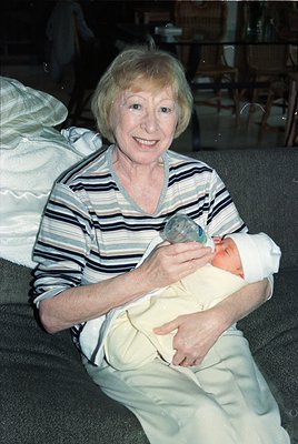Mid-20th century portrait of an elderly woman cradling a newborn, likely from the 1960s–1970s. She wears a striped blouse and...