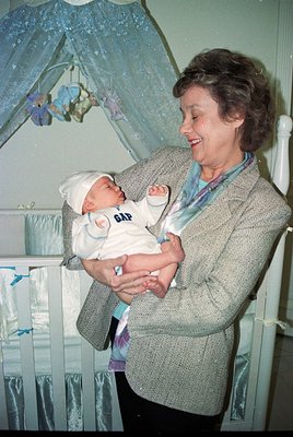 A woman in a 1960s-style sweater cradles a newborn in a hospital bassinet, wearing a diaper with "GAP" branding. Decorative m...