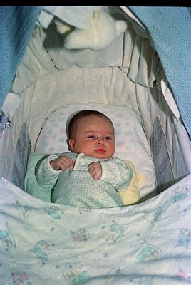 Vintage baby in a white fabric playpen with floral-patterned lining, wearing a crocheted cardigan (green/yellow). Soft focus ...