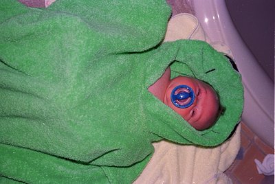 Newborn wrapped in green hospital blanket with blue eye shield, likely for phototherapy. Classic 1970s-1990s neonatal care se...