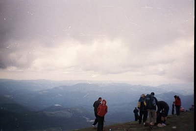 Vintage alpine scene with group of hikers atop a mountain ridge, framed by misty clouds and rolling hills. Distinctive 1980s/...