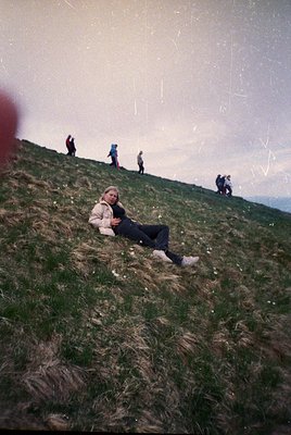 Vintage-style photo of a woman reclining on a grassy hillside, surrounded by hikers in mid-20th century attire. Soft focus an...