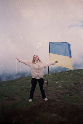 Vintage-style photo of a person holding a Ukrainian flag atop a misty hillside, likely 1980s–1990s. Blue and yellow flag cont...
