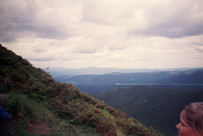 Vintage landscape shot of misty mountain ridges under overcast skies, with a lone road winding through valleys. Foreground sh...