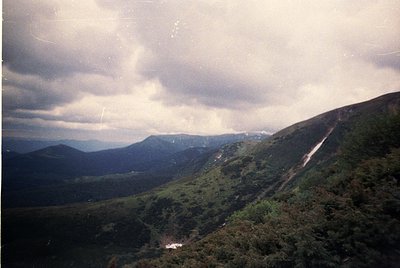 Vintage aerial view of rugged mountainous terrain with dense forest cover. Misty valleys and winding paths suggest remote, un...