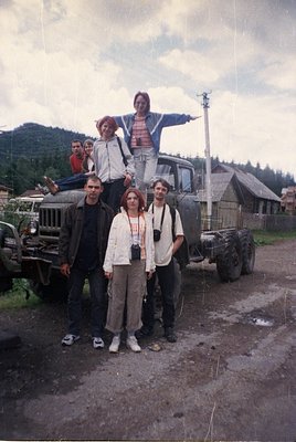 Vintage group photo on a rural dirt road, featuring six individuals posing with a Soviet-era GAZ truck. Three adults stand fr...