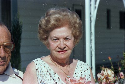 Vintage portrait of an elderly woman with voluminous 1970s-style updo, wearing a floral-patterned sleeveless blouse. Side pro...