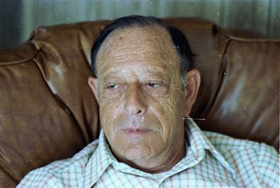 Portrait of an elderly man in a vintage striped shirt, seated on a worn leather couch. The grainy, sepia-toned quality sugges...