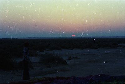 Vintage photograph of a seaside sunset through cracked glass, revealing muted blues and pinks. Distorted reflections create a...