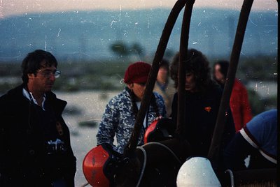 Vintage group photo on a ski lift, likely 1970s–1980s. Four individuals in winter attire—one in a red beret and patterned swe...