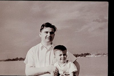 Black-and-white portrait of a man and young boy in outdoor setting, likely mid-20th century. Man wears short-sleeved dress sh...