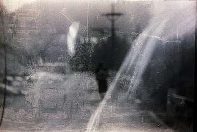 Vintage monochrome photo with heavy vignette and motion blur, likely from a handheld camera. Blurred figures suggest urban st...