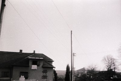 Vintage black-and-white shot of a modest residential building with a tiled roof and chimney, set against a muted landscape. O...