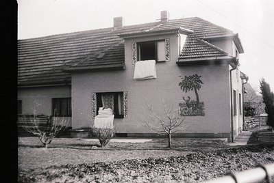 Two-story residential building with decorative plasterwork, likely Eastern European . Red-tiled roof, small front yard with y...