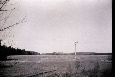 Mid-century rural landscape featuring a tall communication tower in an open field, surrounded by sparse trees and a distant f...