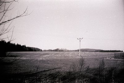 Vintage black-and-white rural landscape featuring plowed fields under an overcast sky. A lone communication tower stands in t...