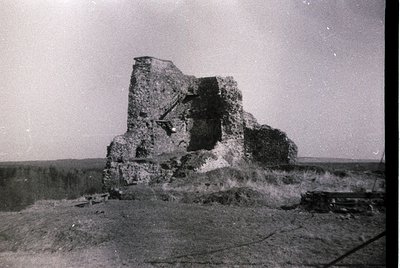 Ruined stone fortress with visible arched entrance and crumbling walls, set in an open landscape. Likely mid-20th century bas...