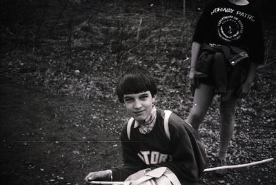 Black-and-white photo of a young boy in a vintage "Toronto" sports jersey, seated outdoors on gravel. Partial view of another...