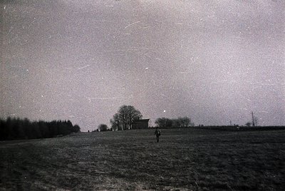 Black-and-white nighttime landscape featuring a lone figure standing in an open field under a starry sky with visible meteor ...