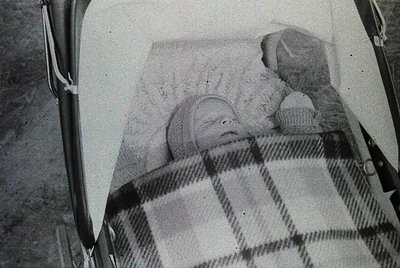 Vintage black-and-white photo of an infant sleeping in a vintage pram with checkered blanket and knitted cap. Cupcake beside ...