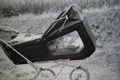 Vintage black-and-white photo of a baby carriage with an open, padded canopy revealing a child inside. Ornate metalwork and a...