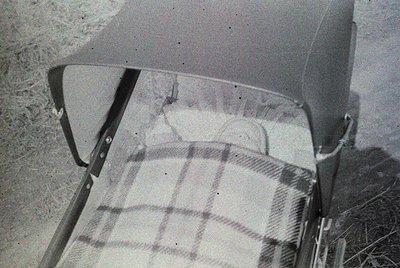 Close-up of a vintage car’s rear passenger seat with a plaid blanket draped over it, suggesting mid-20th century design. Visi...