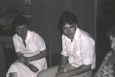 Black-and-white candid of two individuals in casual 1970s attire—women in a sleeveless blouse, men in a button-down shirt—pos...