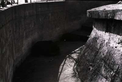 Concrete tunnel entrance with weathered, cylindrical support columns and shadowed interior. Industrial architecture, likely m...