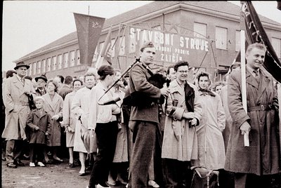 Black-and-white street scene featuring a crowd gathered outside a building with signage in Czech: "Stavební Společnost" (Cons...