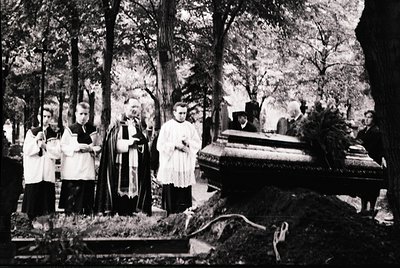 Black-and-white funeral procession in a forested cemetery, likely Eastern European . Clergy in liturgical vestments (cassocks...