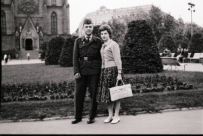 Man in 1950s military uniform (likely Bulgarian People’s Army) poses with woman in patterned skirt and cardigan in a landscap...