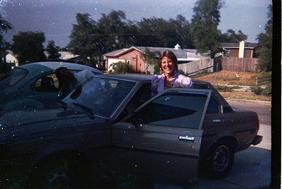 Vintage 1970s-era station wagon with a woman leaning out the driver’s side, smiling. Suburban residential setting with brick ...