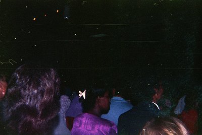Vintage nightclub scene with blurred crowd under disco lighting. Central figure wears a purple shirt and holds a white paper ...