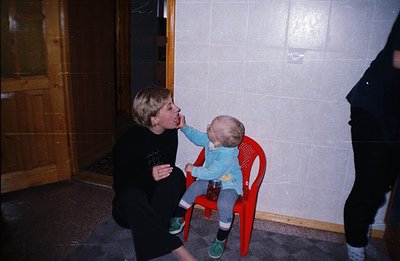 A young girl playfully interacts with a toddler seated in a bright red plastic chair. The scene features textured wallpaper &...