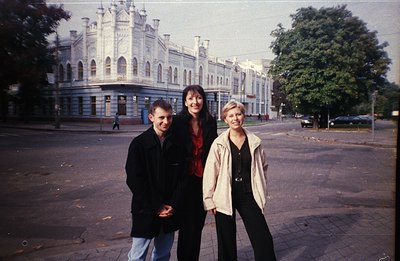 Three people pose in front of a grand, ornate building with numerous arched windows and a central tower, likely government or...