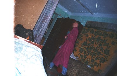 A man in a pink robe and blue jeans stands near a floral-patterned wall, seemingly in a hotel or institutional setting. The r...