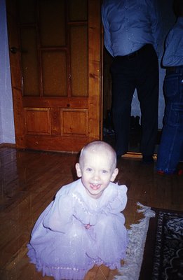 A young child, likely a toddler, is pictured in a playful pose on a patterned rug. They wear a pale blue, ruffled dress and a...