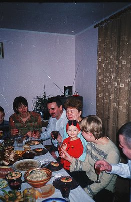 A family gathering captured on film, likely a festive occasion. A large table is laden with food. Guests are seated, enjoying...