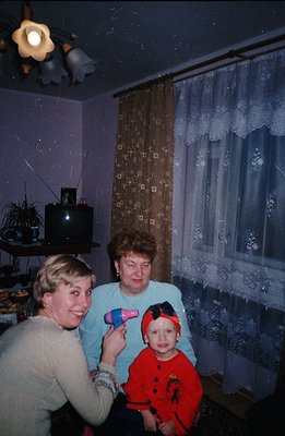 A family portrait in an interior with dated decor—floral curtains, a bulky television, and patterned wallpaper. A young girl ...