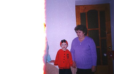 A young child in a red and black costume stands alongside an adult woman within a doorway. The photograph’s dated appearance ...