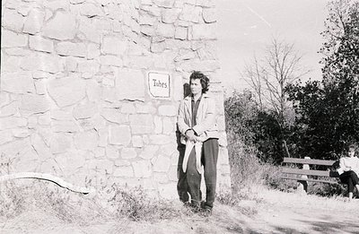 Young man with a layered look stands before a stone wall marked "Tubes." He holds what appear to be bicycle inner tubes. A gi...
