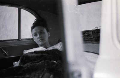 A young woman rests in a closed sleeping berth, likely aboard a train. Sparse, utilitarian interior visible. Appears to be a ...