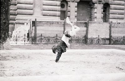 A man mid-fall, captured in a dynamic, candid moment. He's clad in a suit and hat, legs flailing upwards. Architectural backg...