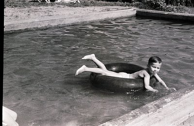 A young boy floats on an inflatable inner tube in a swimming pool. He appears to be paddling with his hands while submerged. ...