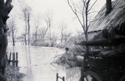 Flooded landscape view with a weathered wooden structure partially visible in the foreground. Bare trees line the water's edg...