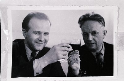 Two men in suits and ties raise glasses of red wine in a formal portrait. Appears to be a studio shot, possibly a business or...