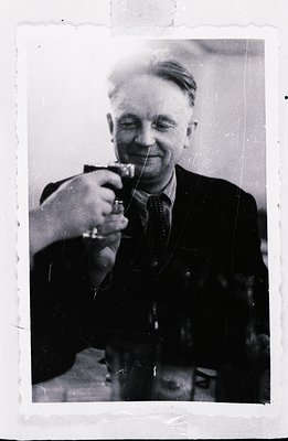 A man in a dark suit and tie raises a glass in a celebratory toast. Appears to be a candid moment, likely indoors. Photograph...
