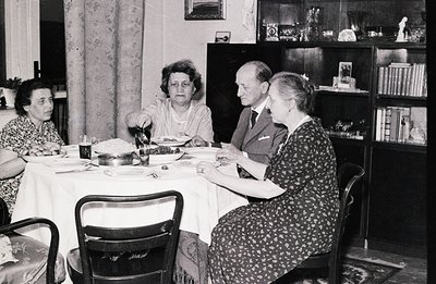 Family gathers around a table laden with food, likely a celebratory meal. The dining room features a built-in bookcase and pa...