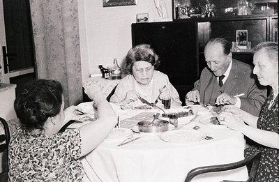 Four individuals seated around a table covered with a white tablecloth, appear to be enjoying a meal. The room features vinta...