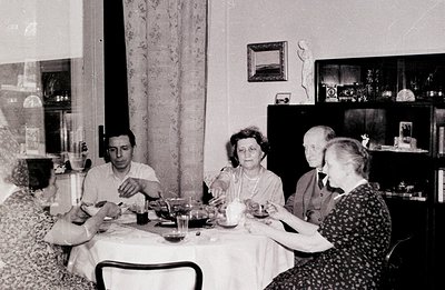 A seated group enjoys a domestic meal, possibly a tea or light lunch. The room features a sideboard, marble bust, and pattern...